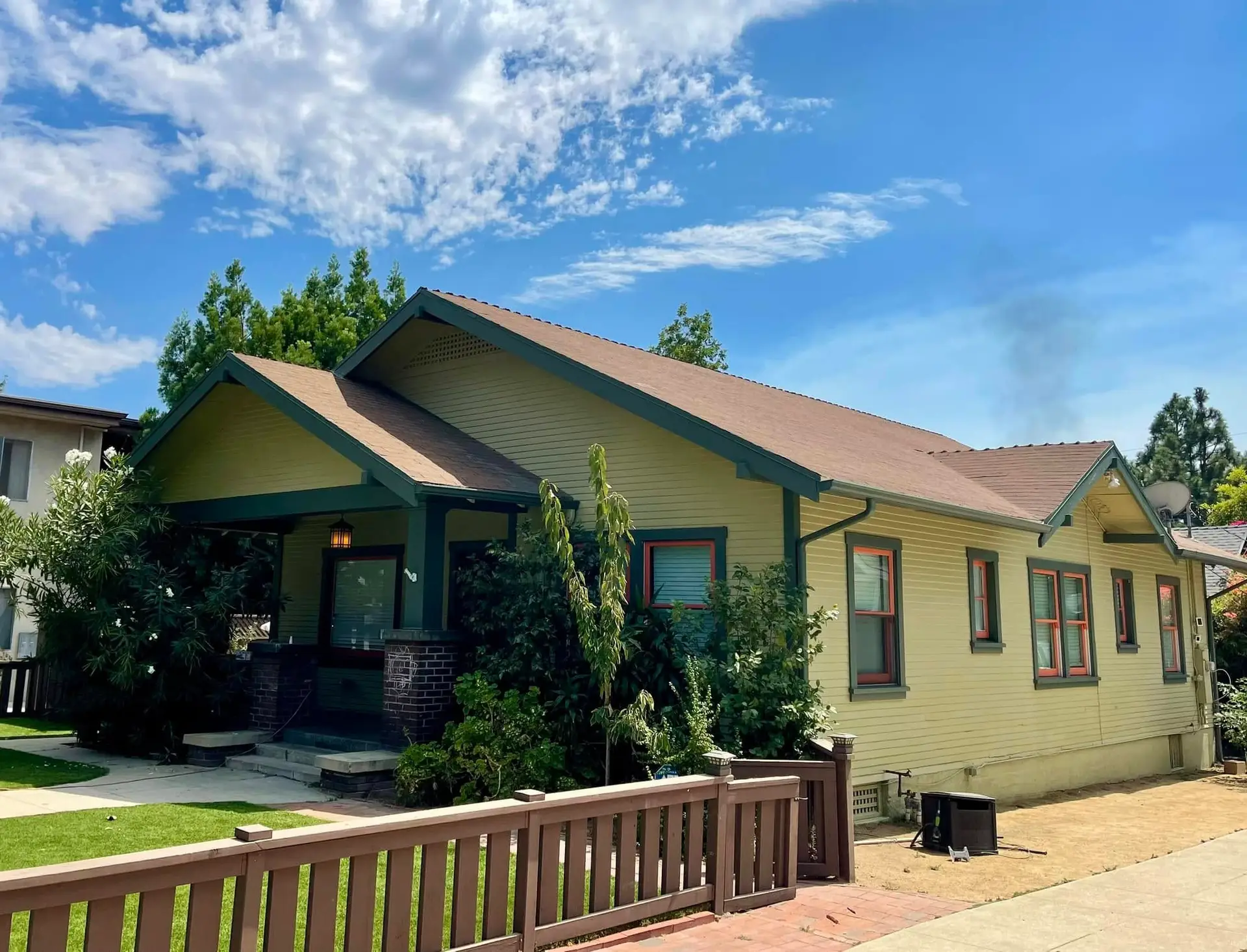 Olive Craftsman bungalow with deep green trim and coral window sashes under wide overhanging eaves
