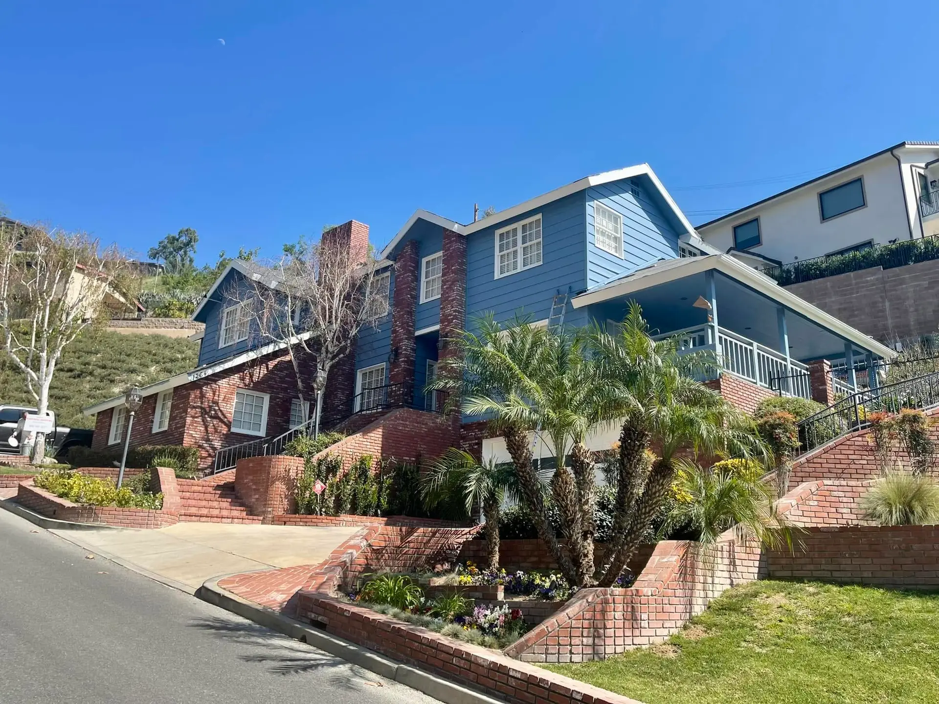 Blue two-story hillside home with brick retaining walls and a covered porch on a foothill street