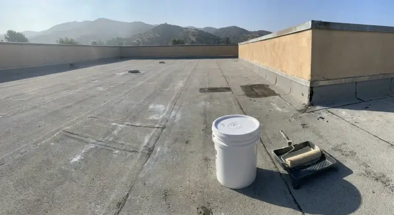 Chalked gray low-slope roof with intact seams beside a parapet wall, ready for elastomeric coating